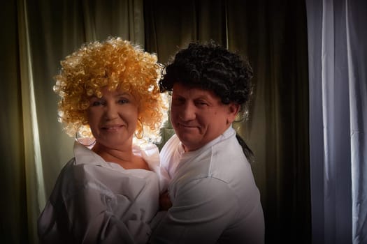 Couple enjoys a playful moment indoors, wearing vintage wigs and celebrating their love through a theatrical photoshoot in their home.