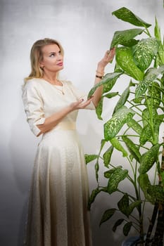 A middle-aged woman with blonde hair showcases her style while interacting with a potted plant indoors.