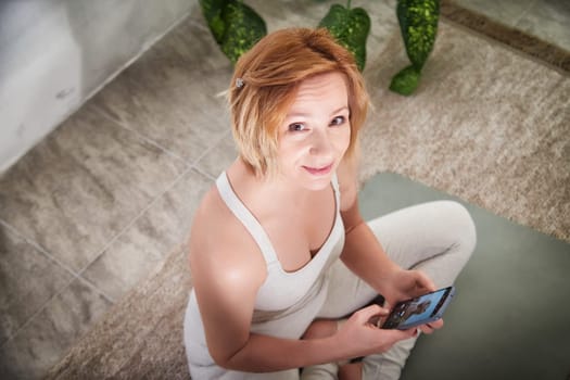 A person seated in a serene yoga space, participating in a wellness routine, connecting with a community via smartphone.