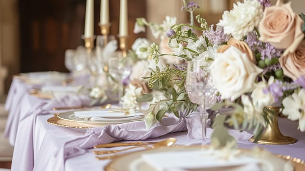 Elegant indoor wedding dining table with floral arrangements in shades of purple, lavender and pink, set in a grand room with mirrors and chandeliers.