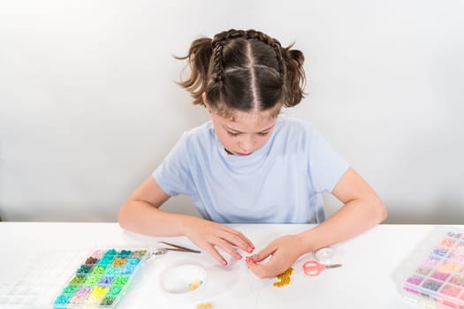 Little girl enjoys crafting colorful bracelets with vibrant clay beads set.
