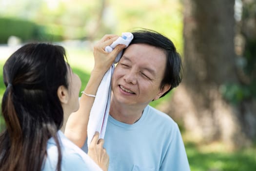 A caring young woman wipes the sweat from a smiling senior man's forehead, emphasizing health and wellness in outdoor activities.