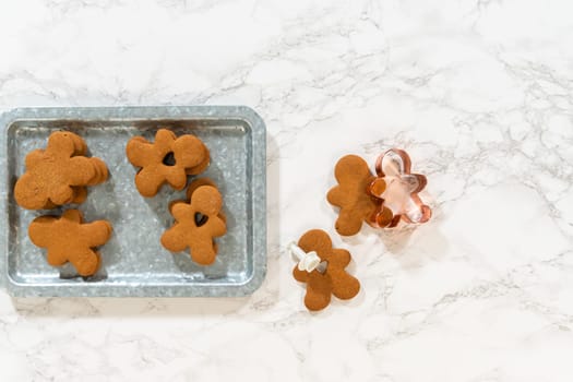 Flat lay. Gingerbread cookies, including a gingerbread man with a heart-shaped cutout, rest on a rustic metal tray against a marble countertop.
