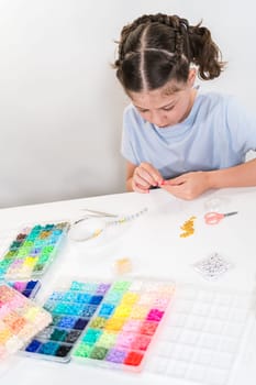 Little girl enjoys crafting colorful bracelets with vibrant clay beads set.
