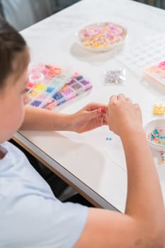 Little girl enjoys crafting colorful bracelets with vibrant clay beads set.