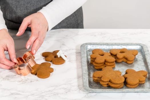 Gingerbread cookies, including a gingerbread man with a heart-shaped cutout, rest on a rustic metal tray against a marble countertop.