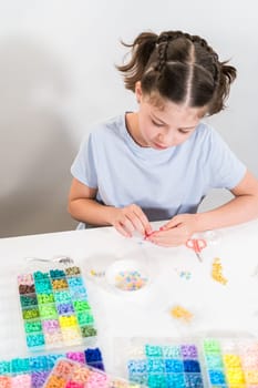 Little girl enjoys crafting colorful bracelets with vibrant clay beads set.