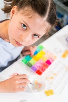 Little girl enjoys crafting colorful bracelets with vibrant clay beads set.