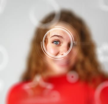 A young woman with curly hair smiles playfully as she peers through a circular, futuristic lens. The background is light, enhancing her joyful expression.
