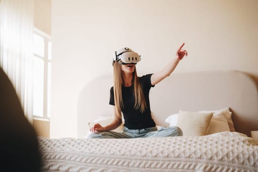 A young woman engages with a virtual reality headset while sitting cross-legged on a bed. Natural light fills the cozy room, creating an inviting atmosphere for her immersive adventure.