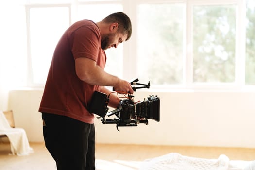 A filmmaker focuses on setting up a camera rig in a well-lit studio. The professional adjusts the settings to prepare for a creative shoot, surrounded by natural light.