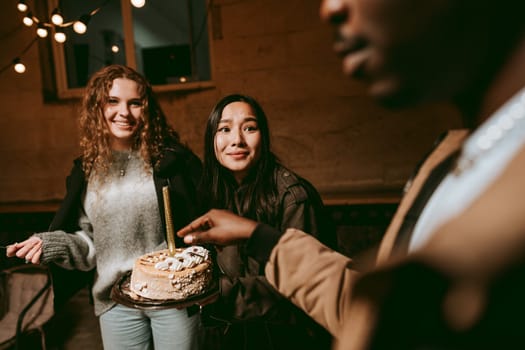 Two friends smile as they celebrate a special occasion, holding a cake with candles. The warm ambiance created by string lights enhances the festive atmosphere.