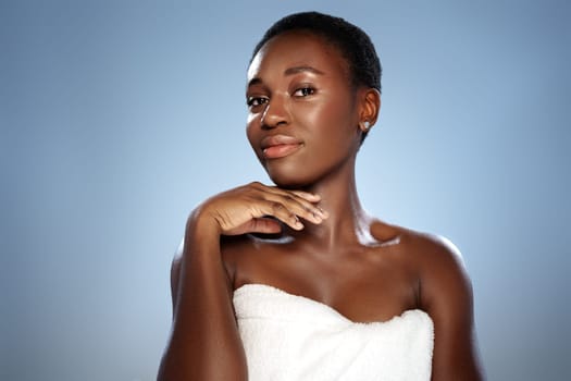 A woman with short hair gracefully poses with her hand near her face, radiating confidence and beauty. The soft blue background enhances her radiant skin tone and charm.