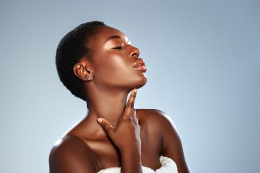 A confident woman with short hair poses against a smooth background, highlighting her radiant skin and elegant demeanor while gently touching her neck in a studio environment.