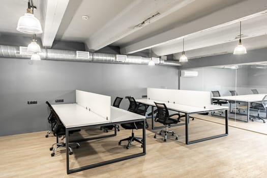 A spacious office area features minimalist desks with ergonomic chairs, large windows providing natural light, and a clean, clutter-free environment suitable for productivity.