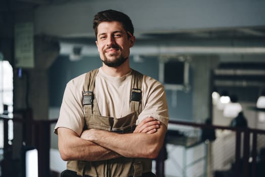 A confident young man in work attire stands with arms crossed in a contemporary indoor environment. Natural light highlights the vibrant workspace, showcasing his professionalism.