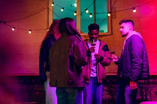 In a lively outdoor setting, a group of friends shares drinks and laughter under vibrant string lights, creating a festive evening ambiance.