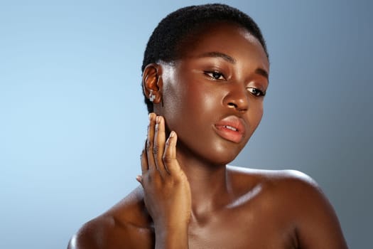 A model showcases her natural beauty with an elegant pose, her hand gently touching her face. The soft blue background enhances her radiant skin tone, creating a calm atmosphere.
