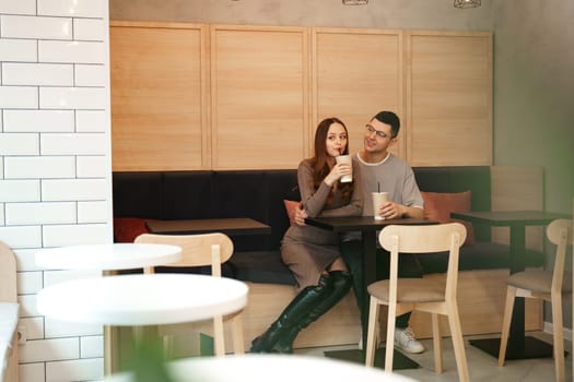 A couple sits together in a contemporary cafe, sipping beverages and engaging in warm conversation. The atmosphere is relaxed and inviting, perfect for a casual outing.