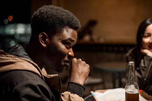 Friends gather in a dimly lit cafe, sharing conversation and laughter. One person enjoys a drink while listening attentively, creating a warm atmosphere.