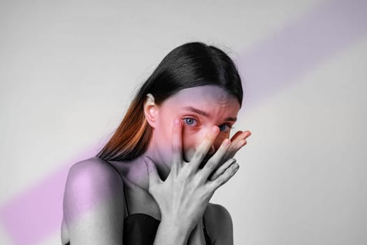 A model expresses vulnerability by covering her face with her hands. The contrast of black and white skin tones mixes with vibrant light patterns, enhancing the emotional depth captured in the moment.