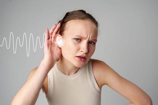 A young woman is focused on a sound wave emanating from her ear, conveying a sense of curiosity and attention in a simple gray background. Her expression shows thoughtfulness.