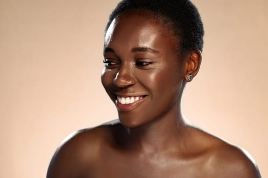 A woman with short, natural hair smiles warmly, exuding confidence and joy. Her skin glows under soft lighting, creating an inviting and uplifting atmosphere.