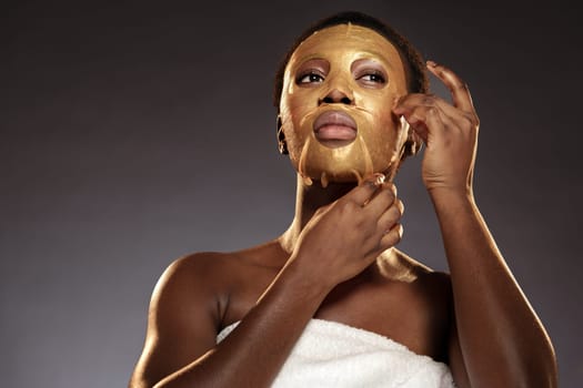 A woman is gently removing a gold facial mask while wrapped in a towel. The setting has a calm, soothing atmosphere, ideal for skincare and relaxation.