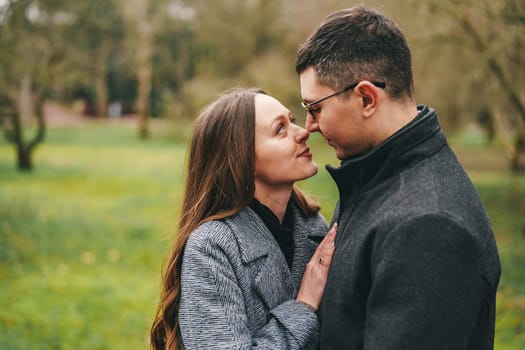 A couple stands closely together in a vibrant green park, gazing into each other's eyes with warmth and affection, enjoying a sunny afternoon surrounded by nature.