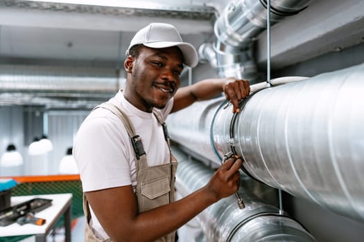 A technician wearing a cap and work overalls tightens a fitting on a large metal pipe in an industrial setting, showcasing expertise and focus on the task at hand.