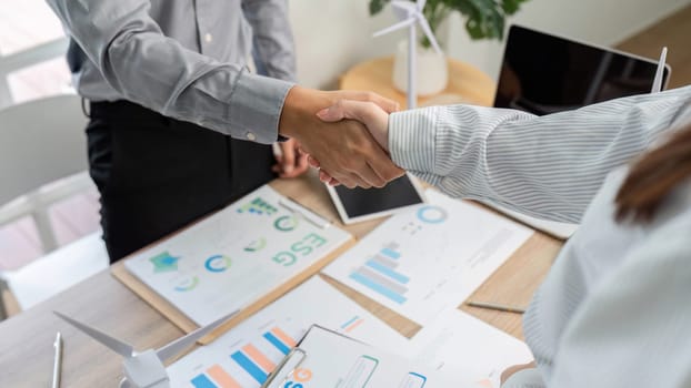 Two professionals shaking hands over ESG documents, representing a commitment to sustainable business practices.