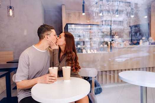 A young couple enjoys their time at a cafe, sitting at a small table with iced drinks. They share a kiss, creating a romantic atmosphere in the cozy setting.