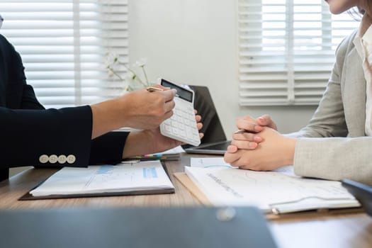A financial consultant explains budgeting strategies to a client, utilizing a calculator in a collaborative office environment.