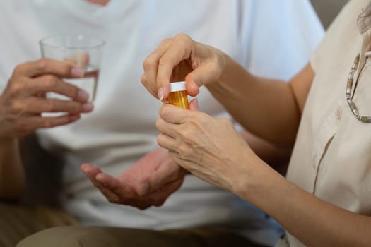 An elderly couple discussing medication management while holding a pill bottle and a glass of water, emphasizing wellness and support.