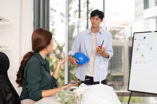 A female engineer engages in conversation with her male colleague, discussing project plans in a vibrant office environment focused on collaboration and innovation.