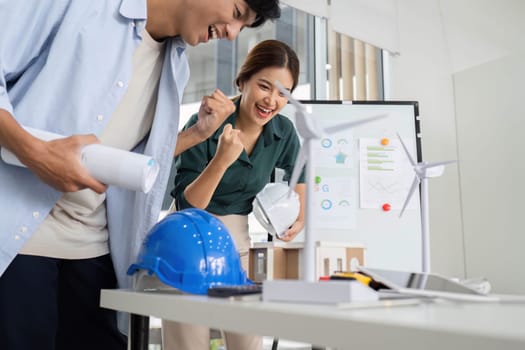 Two professionals enthusiastically examining models and plans for renewable energy solutions in a modern workspace.
