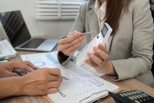 A financial consultant details financial metrics and strategies to a client using a calculator in a collaborative office setting.