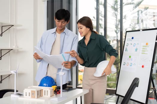 Two engineers review project plans focused on ESG principles, showcasing teamwork and sustainability in architecture.