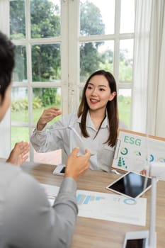A businesswoman enthusiastically presenting ESG metrics and sustainability strategies to her colleague in a bright office.