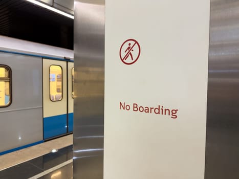 Clear warning sign with red icon and the words No Boarding inside modern subway station, with train stopped nearby. Concept of safety, transportation rules and restricted access area