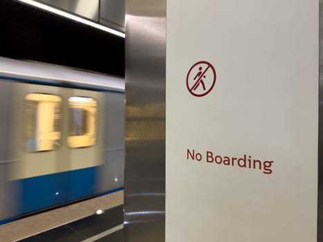 High speed subway train passing by No Boarding sign in modern underground station. Urban transit safety, restriction and public transportation concept with motion blur effect