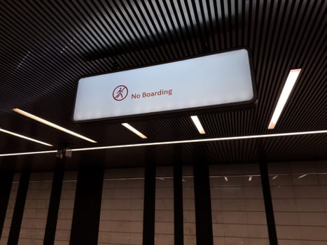 Well lit modern metro station interior with large illuminated No Boarding sign hanging from the ceiling, emphasizing rules and structure in urban public transportation spaces