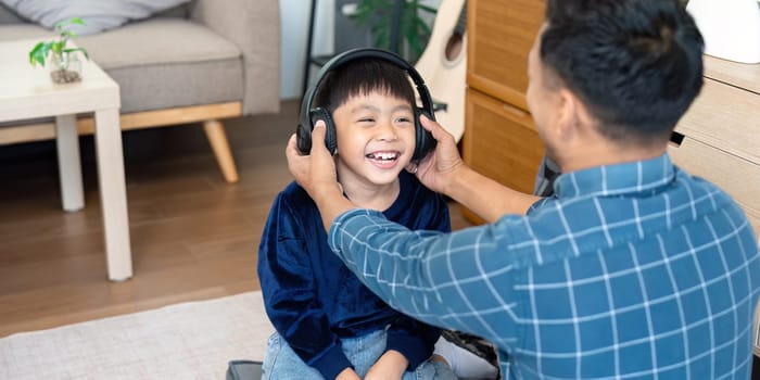 The father assists his son with headphones, enhancing his learning experience at home. Their shared laughter signifies the joy of learning together as school approaches.