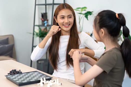 A mother and her daughter engage in a playful chess match, highlighting their strong bond and the joy of family time spent together.