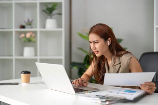 A young woman furrows her brow as she reviews her laptop screen, tackling challenges in her work environment while seeking solutions with determination.