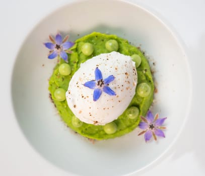 A fresh pea puree is beautifully plated, featuring a poached egg at the center and adorned with borage flowers. The dish showcases vibrant colors and textures, perfect for any spring menu.