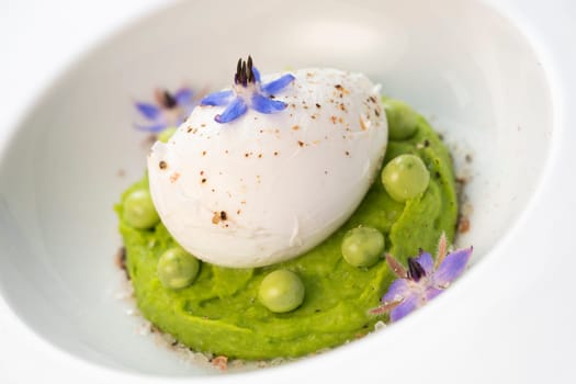 A fresh pea puree is beautifully plated, featuring a poached egg at the center and adorned with borage flowers. The dish showcases vibrant colors and textures, perfect for any spring menu.