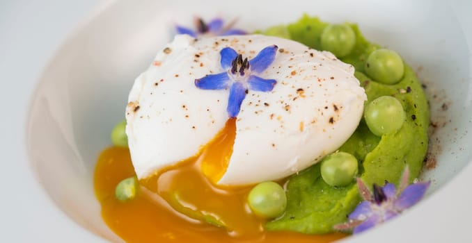 A fresh pea puree is beautifully plated, featuring a poached egg at the center and adorned with borage flowers. The dish showcases vibrant colors and textures, perfect for any spring menu.