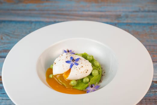 A fresh pea puree is beautifully plated, featuring a poached egg at the center and adorned with borage flowers. The dish showcases vibrant colors and textures, perfect for any spring menu.