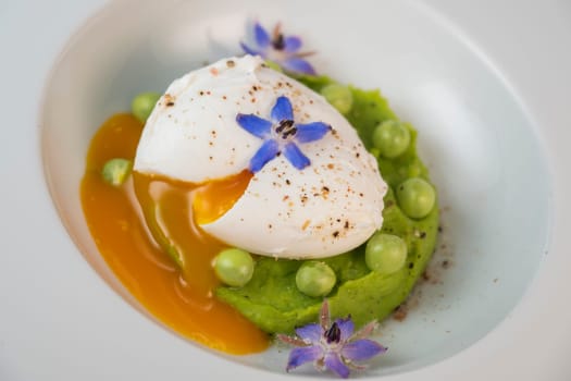 A fresh pea puree is beautifully plated, featuring a poached egg at the center and adorned with borage flowers. The dish showcases vibrant colors and textures, perfect for any spring menu.